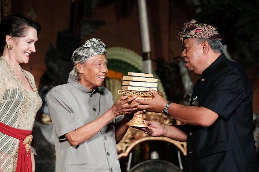 Janet DeNeefe (left) and Dr I Ketut Suardana (right) handing the 2019 Lifetime Achievement Award to I Made Taro